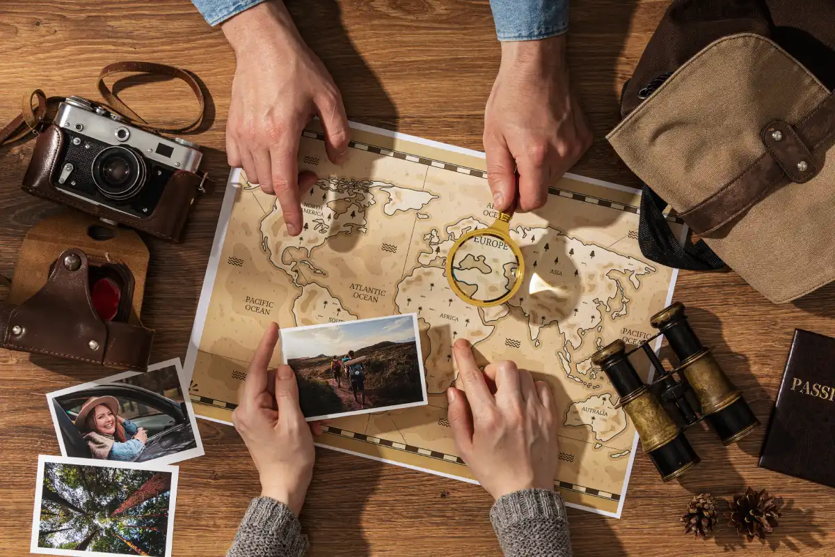 Travelers exploring a vintage map with a magnifying glass, camera, binoculars, and travel photos while planning a treasure-hunting trip.